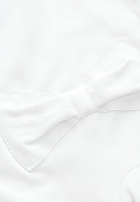 Biała tkanina z wyraźnym detalem kokardy na środku. Gładka faktura z prostymi przeszyciami wokół kokardy.