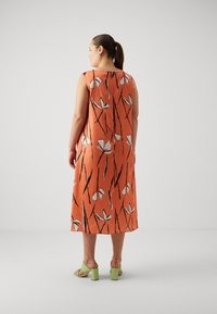 Oranje midi-jurk met een bloemenpatroon en zwart-witte accenten. Mouwloos ontwerp met een ontspannen pasvorm en een zachte stofstructuur.