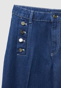 Pantaloni in denim con vita alta, di colore blu scuro, e cinque bottoni metallici lungo il lato sinistro. La texture è liscia con una leggera sfumatura.