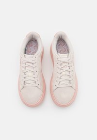 Paire de baskets en daim beige avec semelles et lacets rose clair, vues de dessus sur un fond blanc.