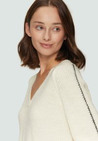 Witte gebreide trui met een V-hals en gestructureerde stof. Heeft een zwarte streep langs de mouw. Zacht, casual ontwerp dat ideaal is voor het combineren met andere kleding.