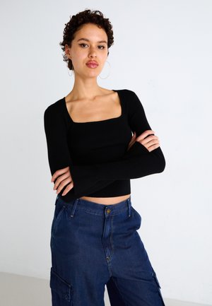 Black ribbed long-sleeve top with a square neckline, paired with blue cargo pants featuring side pockets and a fitted waist.