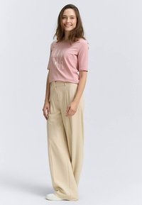 Pink short-sleeved t-shirt with a graphic print, paired with beige wide-leg trousers and white sneakers, featuring a relaxed fit.