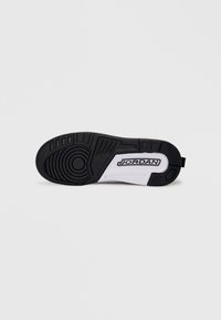 Melnas gumijas sneaker apakšdaļa ar baltām akcents, ar apļveida rakstu un teksturētu detaļu. Redzama "JORDAN" logo.
