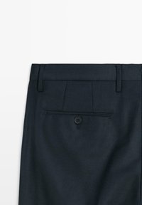 Pantaloni eleganti blu navy scuro vista posteriore con tasca a filetto con bottone e passanti per cintura su sfondo bianco semplice.