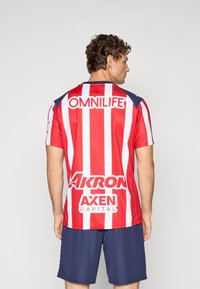Rød og hvit stripete trøye med rund hals, med blå detaljer på skuldrene og flere sponsorlogoer på baksiden.