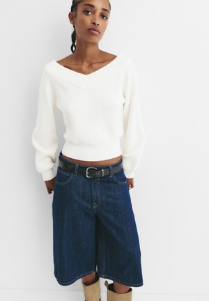 Maglione bianco a costine con scollatura a V ampia, abbinato a culotte in denim blu scuro e una cintura nera con un design di fibbia semplice.