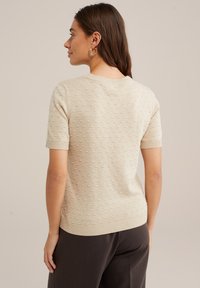 Bēša īsu piedurkņu džemperis ar teksturētu punktu rakstu un ribotām malām. Adīts audums ar gludu apdari, ar apaļu kakla izgriezumu.