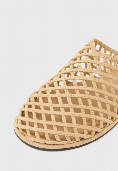 Sandale en cage en matériau synthétique beige avec un design ouvert, dotée d'une texture tissée et d'une semelle noire.