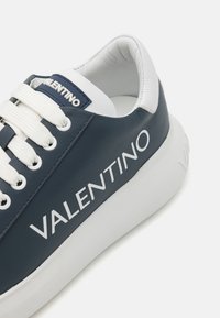 Marine leren sneaker met witte accenten, met een textuur, opvallende branding en ronde veters. Dikke witte rubberen zool.