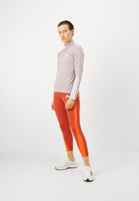 Heledad lilla sportlik üleminek, millel on valged triibud. Punased legginsid oranžide külgpanelidega. Valged spordijalatsid mustade aktsentidega.