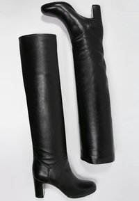 Bottes noires hautes en cuir lisse, avec un talon bloc et un tige ajustée. Le design est épuré avec un hardware minimal.