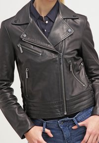 Black leather motorcycle jacket with asymmetrical zippers, snap collar, and ribbed waist detailing, showcasing a fitted silhouette.