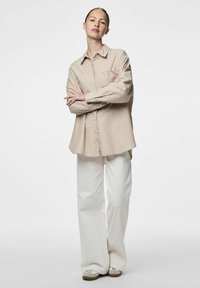 Camicia button-up a strisce color beige chiaro, con vestibilità relaxed e maniche lunghe, abbinata a pantaloni bianchi larghi e scarpe beige.