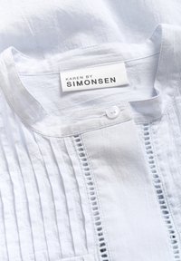 Camicia bianca con pieghe a pintuck e dettagli in pizzo; presenta un collo rotondo e una chiusura a bottoni; realizzata in un tessuto leggero e strutturato.