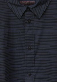 Krátký rukáv námořnické modré košile vyrobené z hladké látky, s jemným vodorovným pruhovaným vzorem v tmavších odstínech, klasickým límcem a zapínáním na knoflíky.