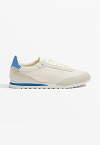 Helle beige Sneaker mit einem glatten Textil-Obermaterial, blauen Akzenten an Ferse und Streifen, strukturiertem Wildleder vorne und einer Gummisohle mit Traktion.