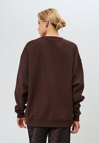 Hnedý nadrozmerný sveter s okrúhlym výstrihom, spadnutými ramenami a rebrovanými manžetami. Mäkka textúra a uvoľnený strih.