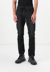 Črne denim hlače z elastiko v pasu, oprijet kroj in dve sprednji žep. Slog preprosta črna majica in črne superge.