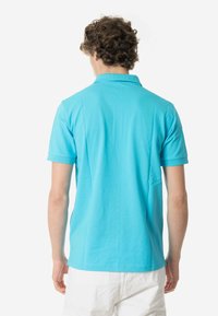 Polo shirt azzurro chiaro realizzato in cotone liscio, con colletto e maniche corte. La vista posteriore mostra un taglio dritto e dettagli minimi.