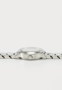 Reloj de pulsera plateado con una caja redonda, pulsera de eslabones de metal y un bisel liso. Incluye una corona de cuerda y una esfera de cristal transparente.