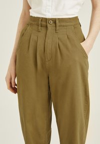 Pantalones de tejido kaki con pliegues, que cuentan con una cintura alta, cierre de botón y bolsillos laterales, confeccionados en una suave y ligera tela.