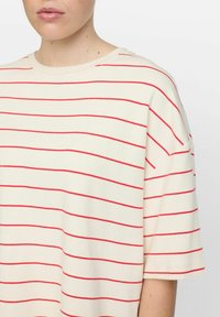 Light cream short-sleeve t-shirt with red horizontal stripes. Features a round neckline and soft, smooth texture. Suitable for casual wear.