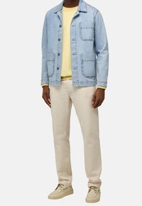 Vaaleansininen farkkutakki, jossa on kaksi etutaskua, kerroksittain keltainen collegetakki alla. Beige housut ja kermaiset kengät viimeistelevät asun.