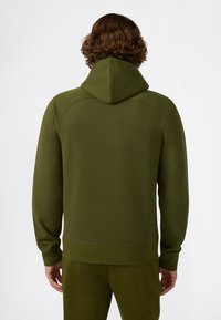 Man met olijfgroene hoodie en bijpassende trainingsbroek, weergegeven van achteren tegen een plain witte achtergrond.