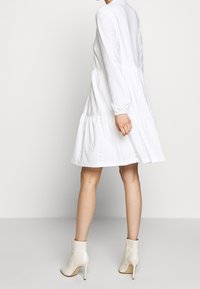 Weißes langärmliges Kleid mit gestuften Rock und Lochmuster. Kombiniert mit cremefarbenen Ankle Boots mit einem Reißverschluss an der Rückseite und Stiletto-Absatz.