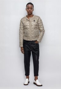 Beige diamant-quiltad jacka med framknäppning, två bröstfickor, svarta byxor och vita slipskor. Slät textur, kort design.