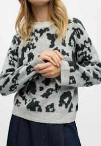 Pull gris avec un motif animal noir, texture tricotée, et poignets et taille côtelés. Le mannequin le porte sur une jupe en denim.