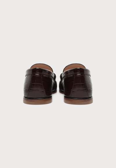 Paire de mocassins marron foncé, brillants, à motif crocodile, vues de dos, avec des semelles marron clair sur fond blanc.