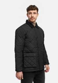 Zwarte gewatteerde jas met ruitpatroon, voorzien van een knoopsluiting, zijzakken en een contrasterende corduroy kraag.