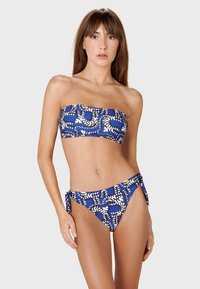Plavi bandeau bikini s geometrijskim bijelim uzorcima. Donji dio ima vezice sa strane, što nadopunjuje dizajn gornjeg dijela. Glatka tekstura.