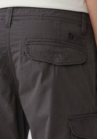Pantalons cargo gris avec un motif en points, poche arrière avec rabat et étiquette de logo sur la taille. Le matériau semble durable avec une texture lisse.