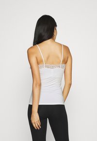 Camisole blanche avec des fines bretelles et une bordure en dentelle le long du décolleté, assortie à des leggings noirs, vue de dos.