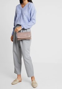 Pull tricot bleu clair avec un col en V, pantalon gris fuselé et chaussures beige à enfiler. Comprend un petit sac à main tissé avec une bandoulière chaîne.