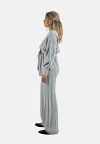 Completo loungewear grigio a maglia con una texture a coste, pullover oversize con spalle scese e pantaloni a gamba larga. Calzature nere in mostra.