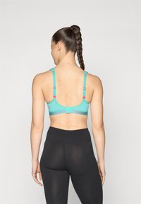 Sport-BH i teal med nettingpaneler, justerbare stropper med rosa detaljer og krok-lukking bak. Sorte høyt liv leggings.