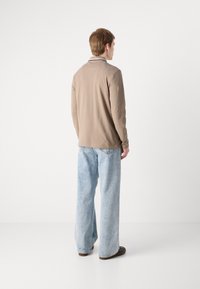 Camisa polo de manga longa bege com colarinho, combinada com jeans de perna larga azul-claro e sapatos escuros. Tecido suave com um corte descontraído.