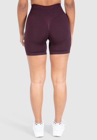 Shorts deportivos de talle alto burdeos con un patrón texturizado y un diseño ajustado, combinados con zapatillas blancas.