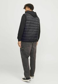 Schwarze Steppweste mit horizontaler Steppung, getragen über einem schwarzen Langarmshirt und grauen, weiten Jeans mit Taschen.