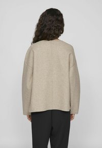 Beige, oversized tröja med sjunkna axlar och rundad halsringning. Mjuk, texturerad tyg med en enkel, oansträngd design.