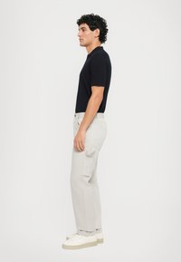 Zwart poloshirt met korte mouwen, lichtgrijze cargobroek met zijzakken, en witte sneakers met een dikke zool. Schoon en minimalistisch ontwerp.