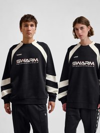 Two people wearing black and white SWARM Internationals sweatshirts and black pants, standing against a plain light background.