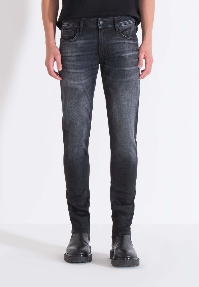Schwarze Denim-Jeans mit einem ausgewaschenen Finish, schlankem Schnitt, Fünf-Tasche-Stil und Gürtelschlaufen. Getragen mit schwarzen Knöchelstiefeln.