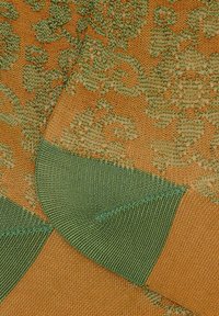 Tessuto lavorato a maglia con un motivo floreale nei toni del verde e dell'arancione. Textura liscia con cuciture verdi in contrasto sui bordi.