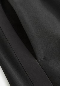 Tissu noir présentant une texture lisse et des tissages variés. Comprend une bande brillante contrastante et des coutures soignées le long des bords.
