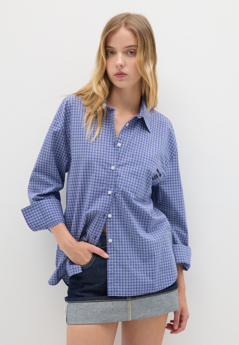 Camicia a quadri blu e bianca con colletto button-down, maniche lunghe e vestibilità rilassata, abbinata a una minigonna di jeans.